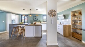 Una cocina moderna con una isla central, iluminación colgante y un reloj en la pared.