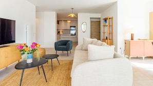 Ein modernes Wohnzimmer mit Sofa, Couchtisch, Fernseher und einer Küche im Hintergrund.