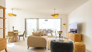 Ein modernes Wohnzimmer mit Sofa, Sesseln, Fernseher und Essbereich.