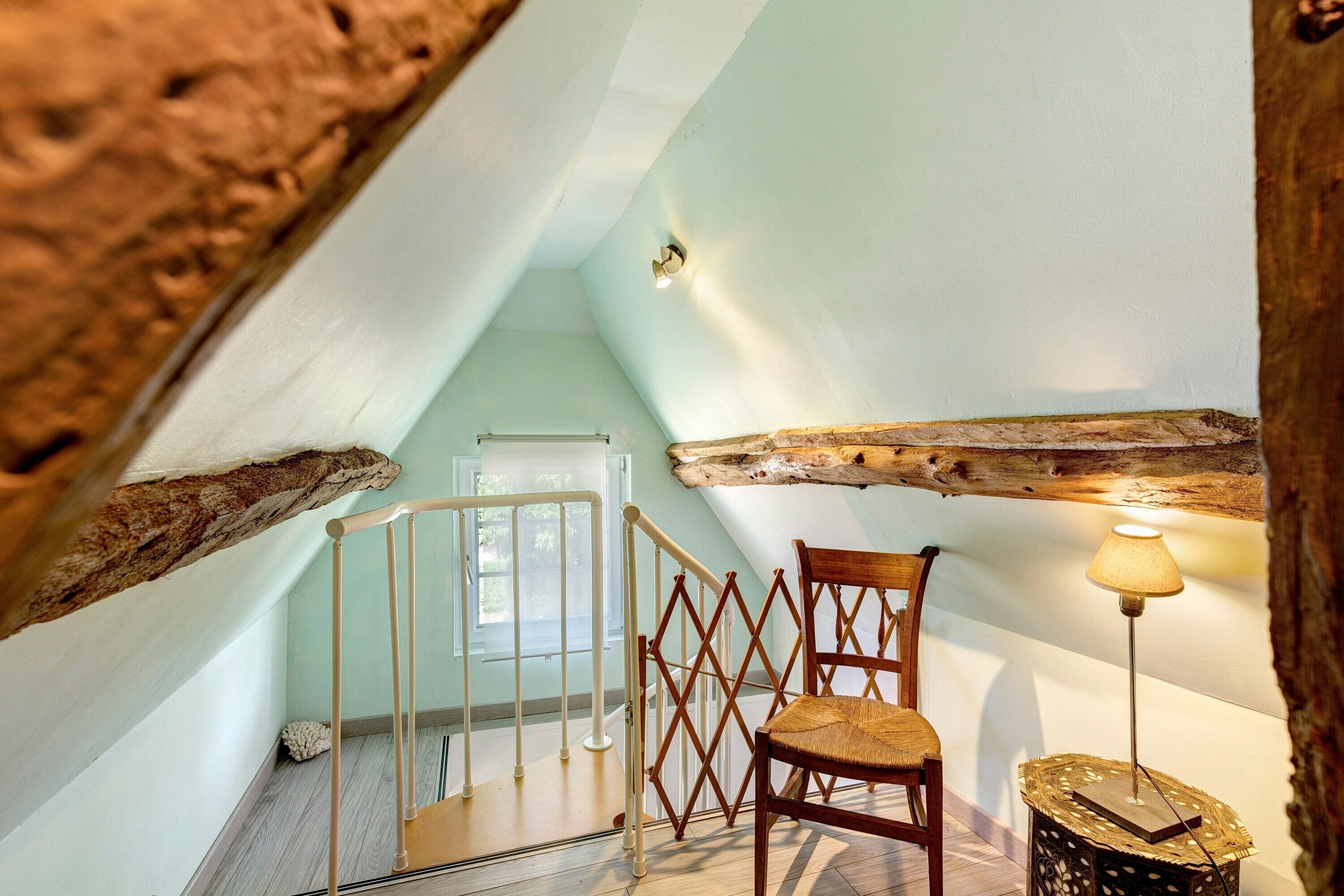 Une pièce avec un plafond en bois, une chaise, une lampe et un escalier.