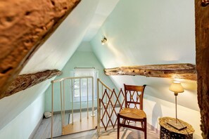 A room with a wooden ceiling, a chair, a lamp, and a staircase. - Holiday Home 'La Petite Chaumière' with Shared Garden (Sainte-Foy)
