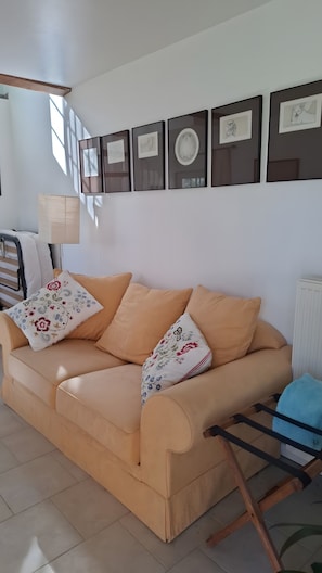 Ein beiges Sofa mit floralen Kissen, ein Holzstuhl und gerahmte Kunstwerke an der Wand.