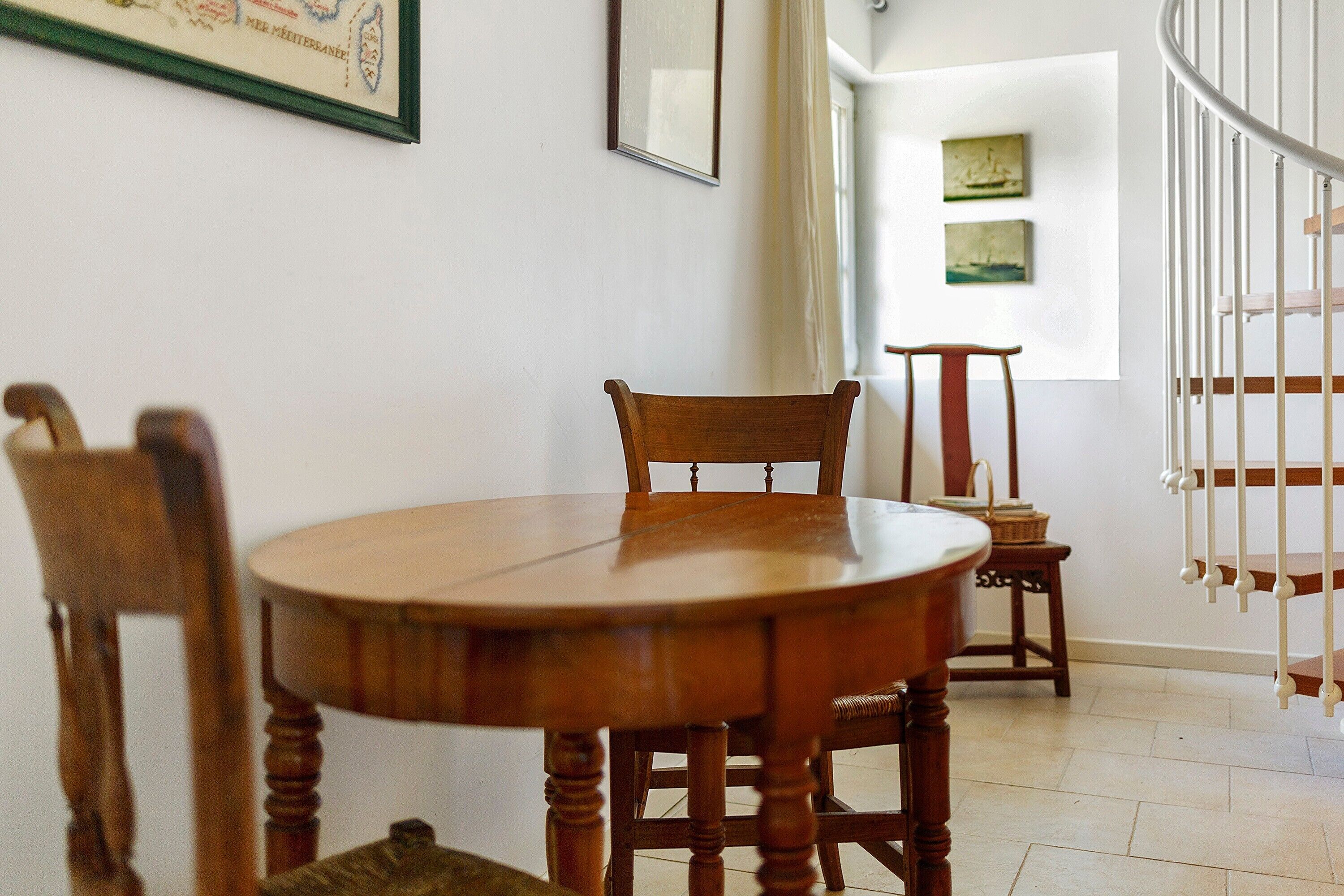 Een eetruimte met een houten tafel en stoelen, een trap en kunstwerken aan de muren.