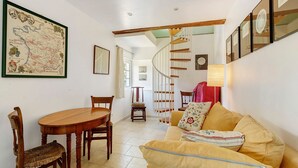 A dining area with a wooden table and chairs, a map on the wall, a staircase, and a sofa with cushions. - Holiday Home “La Petite Chaumière” with Shared Garden (Sainte-Foy)