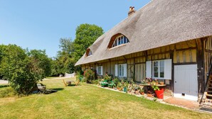 A traditional half-timbered house with a thatched roof, a well-maintained garden, and outdoor seating. - Holiday Home “La Petite Chaumière” with Shared Garden (Sainte-Foy)