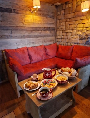 Una habitación acogedora con un sofá de madera, una mesa con alimentos para el desayuno y paredes de piedra.