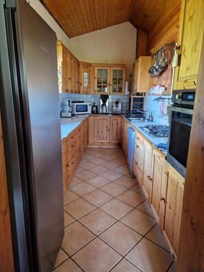 A narrow kitchen with wooden cabinets, a tiled floor, and basic appliances. - Les Chryolles - The springs (Valmeinier)
