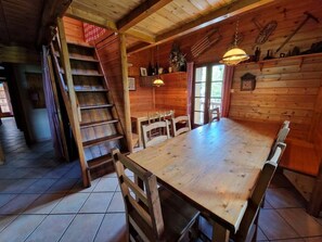 A wooden interior with a dining table, chairs, a staircase, and a chandelier. - Les Chryolles - The springs (Valmeinier)