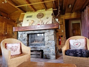 A cozy log cabin interior with a stone fireplace, wicker furniture, and wooden beams. - Les Chryolles - The springs (Valmeinier)