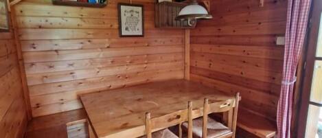 Een houten interieur met een tafel, stoelen, een hanglamp en een raam met gordijnen.