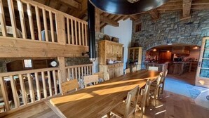 Ein rustikaler Essbereich mit einem langen Tisch und Bänken, Steinwänden und einer im Hintergrund erkennbaren Küche.