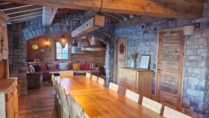 Ein rustikaler Essbereich mit einem langen Holztisch und Stühlen, Steinwänden und einem Kamin aus Stein.