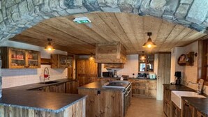 Eine rustikale Küche mit Holzschnitzereien, einer Decke aus Steinbögen und einer zentralen Kochinsel.
