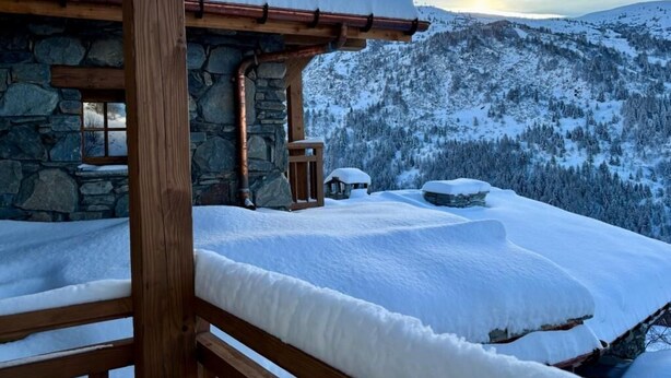 Ein mit Schnee bedeckter Balkon mit einer Steinmauer und einem Holelgeländer.