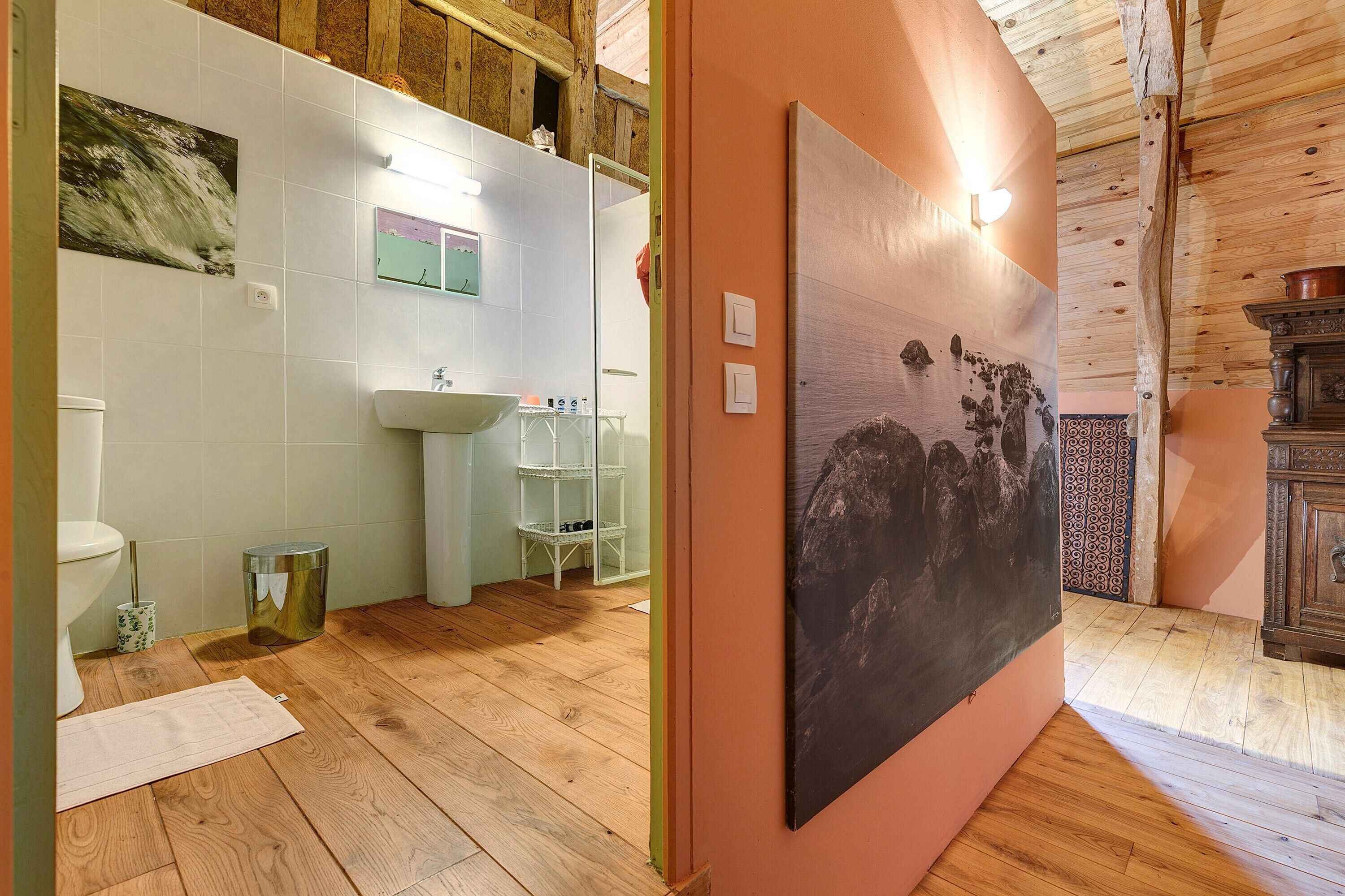A bathroom with a wooden floor, white tiles, a sink, and a mirror.