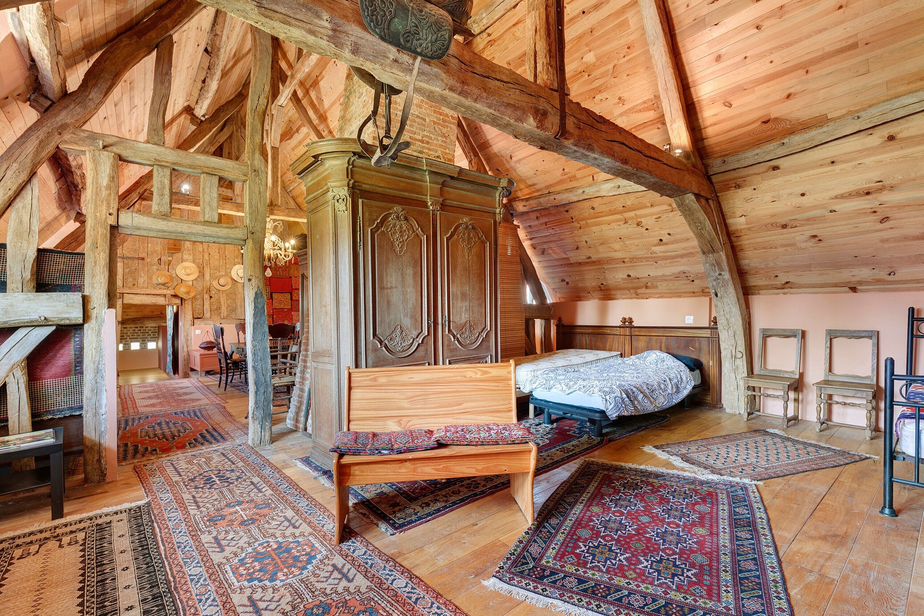 Ein rustikales Schlafzimmer im Dachgeschoss mit einem hölzernen Bett, einer Sitzbank und einem großen Kleiderschrank.