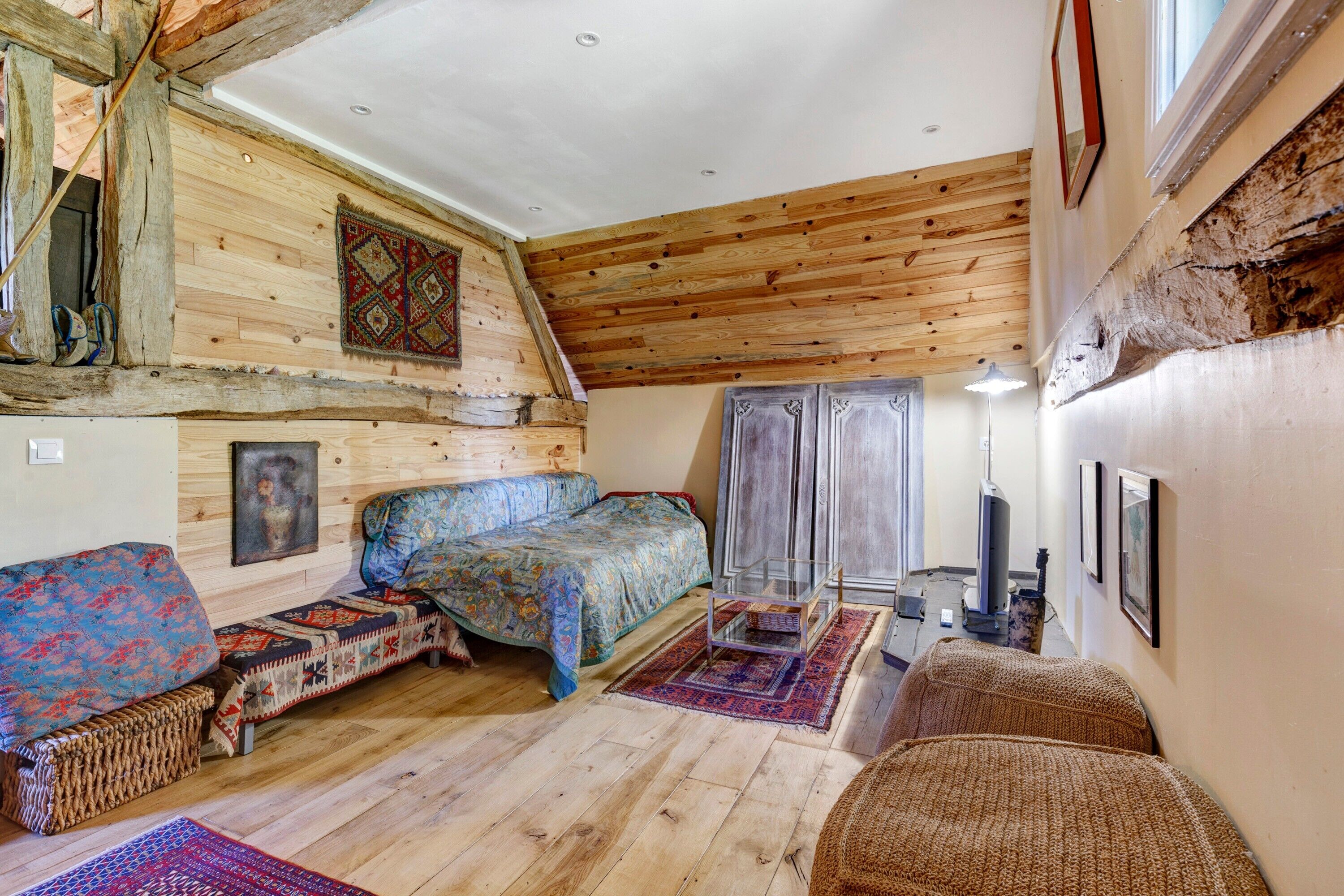 Une pièce rustique en bois, avec un lit, un banc, une petite table et une chaise.