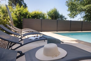 Un espace am énagé au bord de la piscine, avec des chaises longues et un chapeau posé sur l’une d’elles.