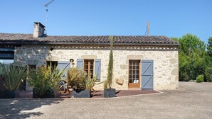 Un edificio de piedra con tejado de tejas, chimenea y camino de grava.