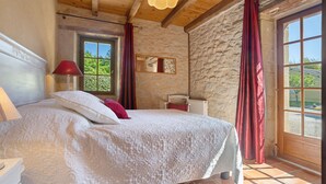 Un dormitorio con una cama grande, paredes de piedra, una ventana con cortinas y un techo de madera.