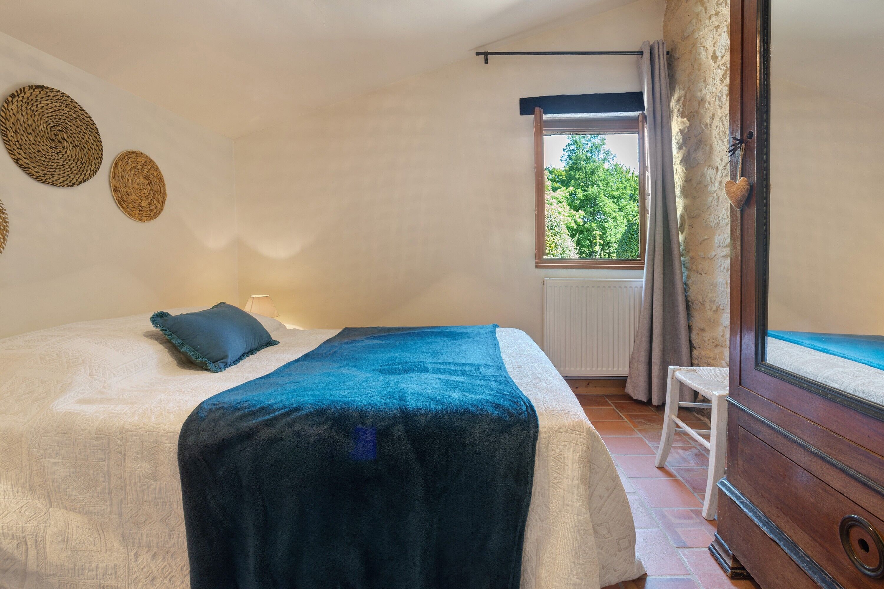 Um quarto com cama, janela com cortinas, radiador e porta de madeira.