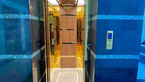 Un ascenseur doté d’une porte en verre, d’un sol à motifs et d’un mur bleu sur lequel est affiché un panneau.