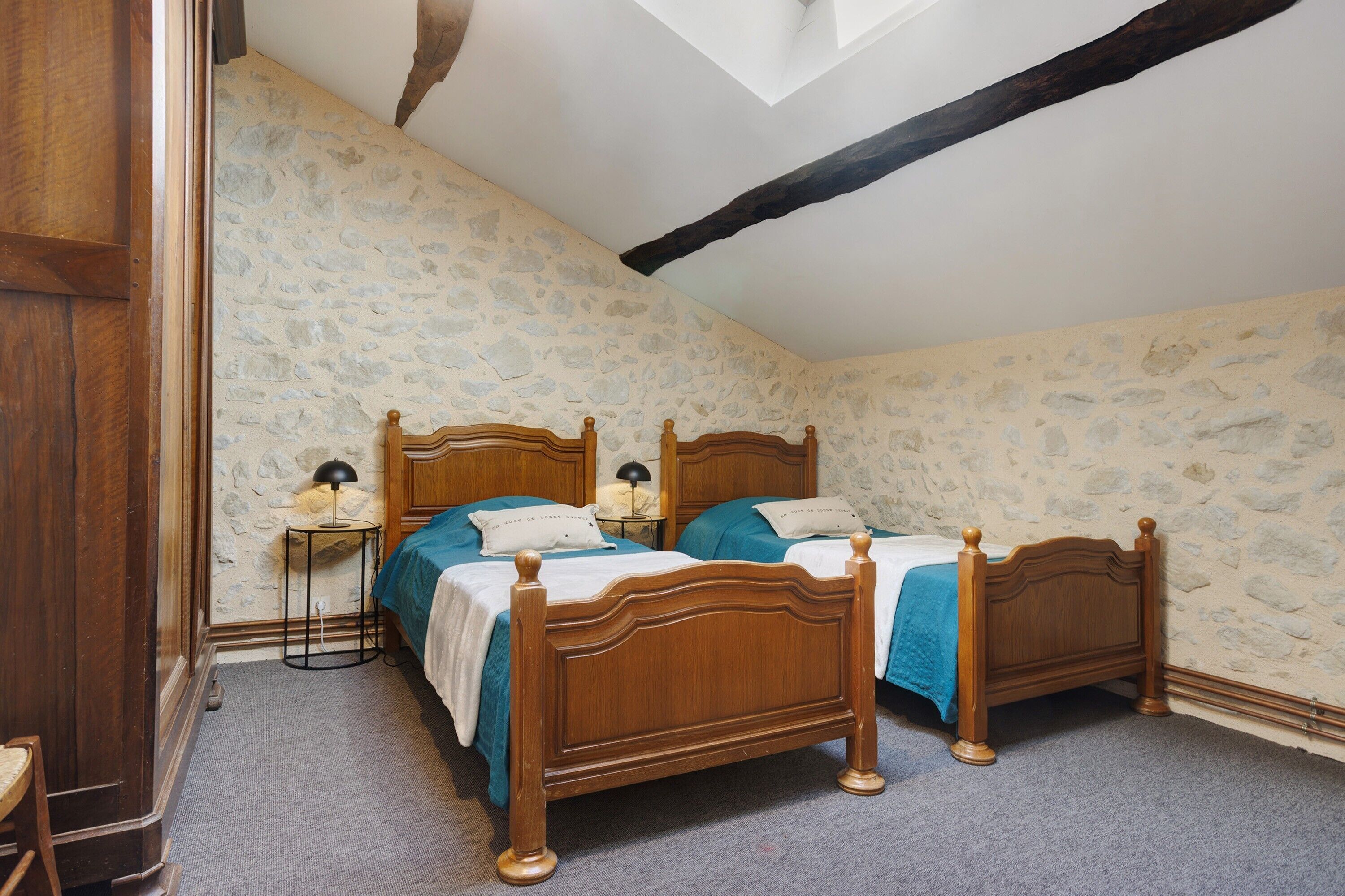 Une chambre à coucher avec deux lits en bois, des murs en pierre, un plafond en pente et un puits de lumière.