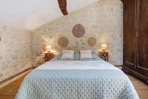 Ein Schlafzimmer mit einer Steinsandsteinwand, einem Bett mit weißer Bettdecke, zwei Nachttischlampen und einem Holzschrank.