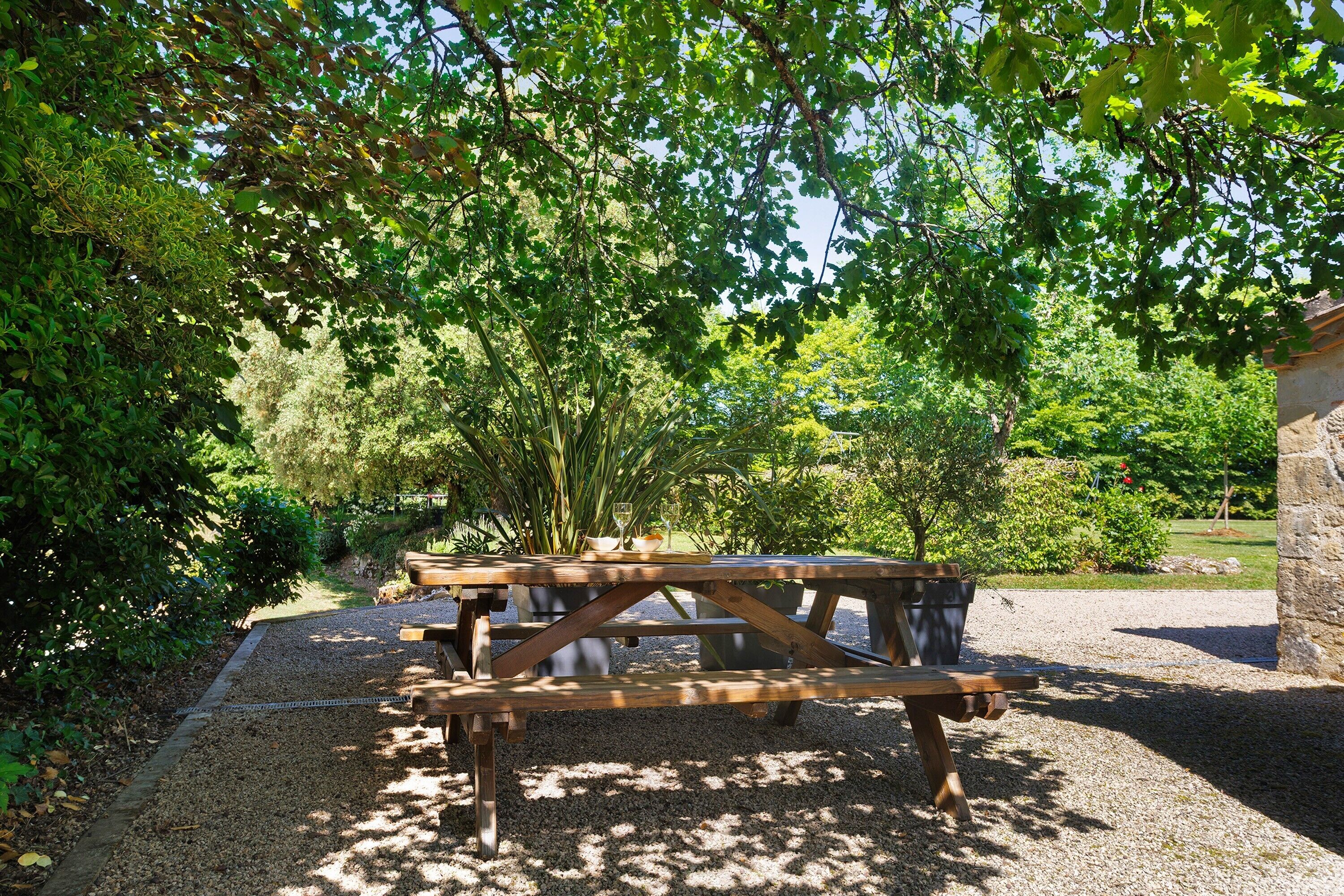 Un tavolo da picnic in un giardino con fondo di ghiaia, circondato da alberi e vegetazione.