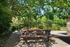 Ein Picknicktisch mit Bänken in einem Garten mit Bäumen und Kies.