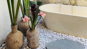 Uma área de spa com parede de pedra, banheira e plantas decorativas.