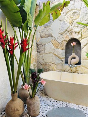 Ein Wellnessbereich mit Steinwand, Badewanne und Zierpflanzen.