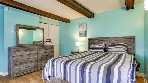 A bedroom with a wooden headboard, a large bed with striped bedding, a dresser, and a mirror. - Near I-95 & Rhode Island Border! Pet-Friendly Home (Attleboro)