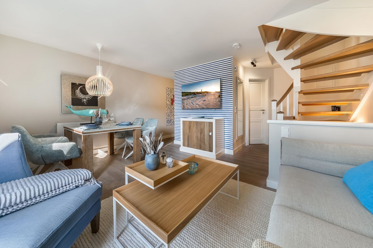A modern living room with a dining area, a staircase, and a view of the outdoors.