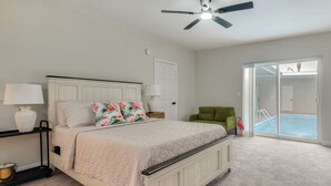 A bedroom with a bed, a nightstand, a lamp, a ceiling fan, a green chair, and a view of a pool through a sliding glass door. - Shuttle Launch Views! Escape 9 Mi to Cocoa Beach (Rockledge)