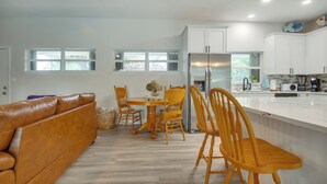 A modern kitchen with white cabinets, a stainless steel refrigerator, and a dining area with wooden chairs and a table. - Shuttle Launch Views! Escape 9 Mi to Cocoa Beach (Rockledge)