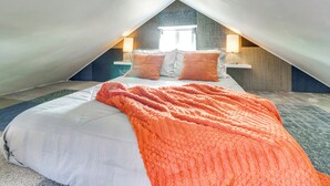 An attic bedroom with a pitched roof, a bed with white bedding and an orange blanket, a nightstand with a lamp, and a window with curtains. - Historic District Studio, 10 Mi to Balloon Fiesta (Albuquerque)