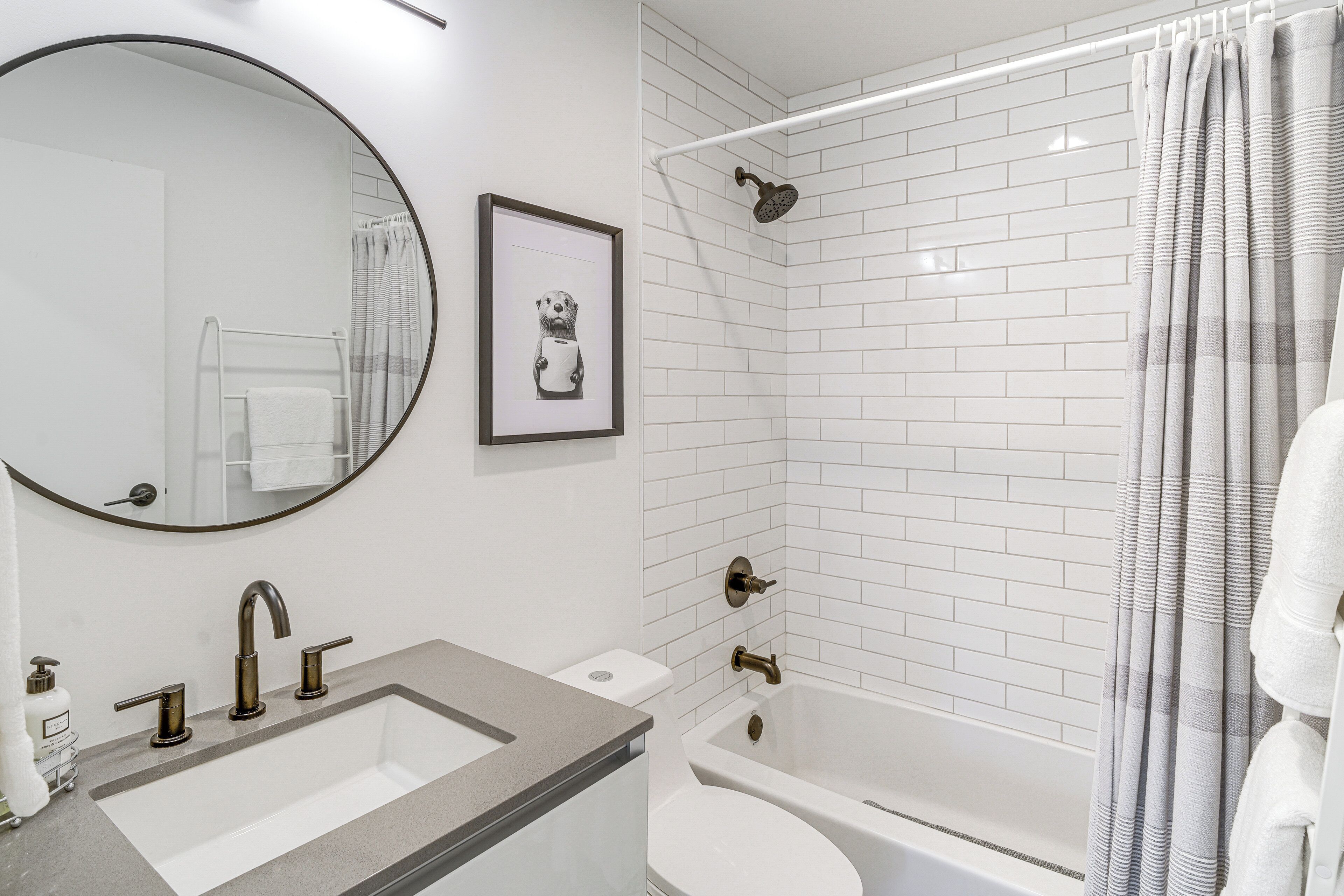 Une salle de bain avec un lavabo, des toilettes et une baignoire, des murs recouverts de carreaux blancs et un tableau encadré au mur.