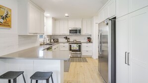A modern kitchen with white cabinetry, stainless steel appliances, and a central island with stools. - Overland Park Home Near Dtwn w/ Easy Hwy Access (Overland Park)