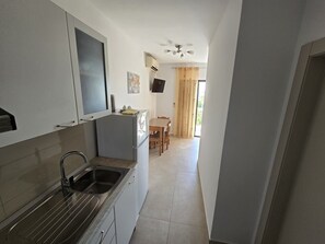 A narrow kitchen with a sink, a refrigerator, and a dining area with a table and chairs. - Studio Apartment Lea (Nin)