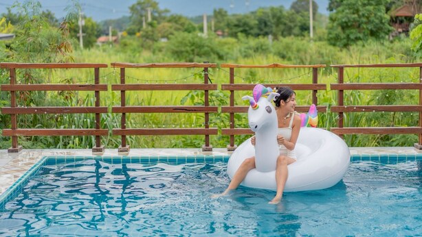 Una piscina con una valla de madera y una persona en un flotador de unicornio blanco inflable.