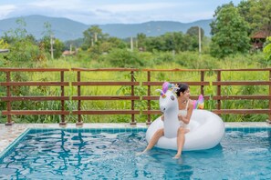 Une piscine entourée d’une clôture en bois, et une personne sur un flotteur en forme de licorne blanche gonflable.
