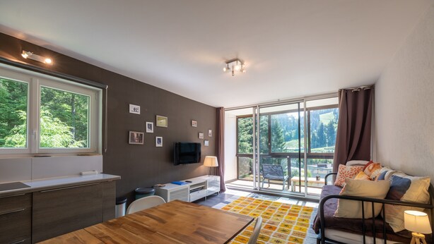 Ein modernes Wohnzimmer mit Esstisch, Sofa, Fernseher und großen Fenstern.