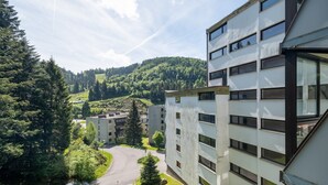 Ein modernes, mehrstöckiges Gebäude, umgeben von üppiger Vegetation und einer hügeligen Landschaft.