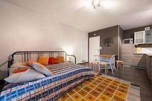 A bedroom with a bed, a desk, and a kitchenette.