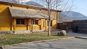 A log cabin with a sloped roof, a stone foundation, and a view of mountains in the background.