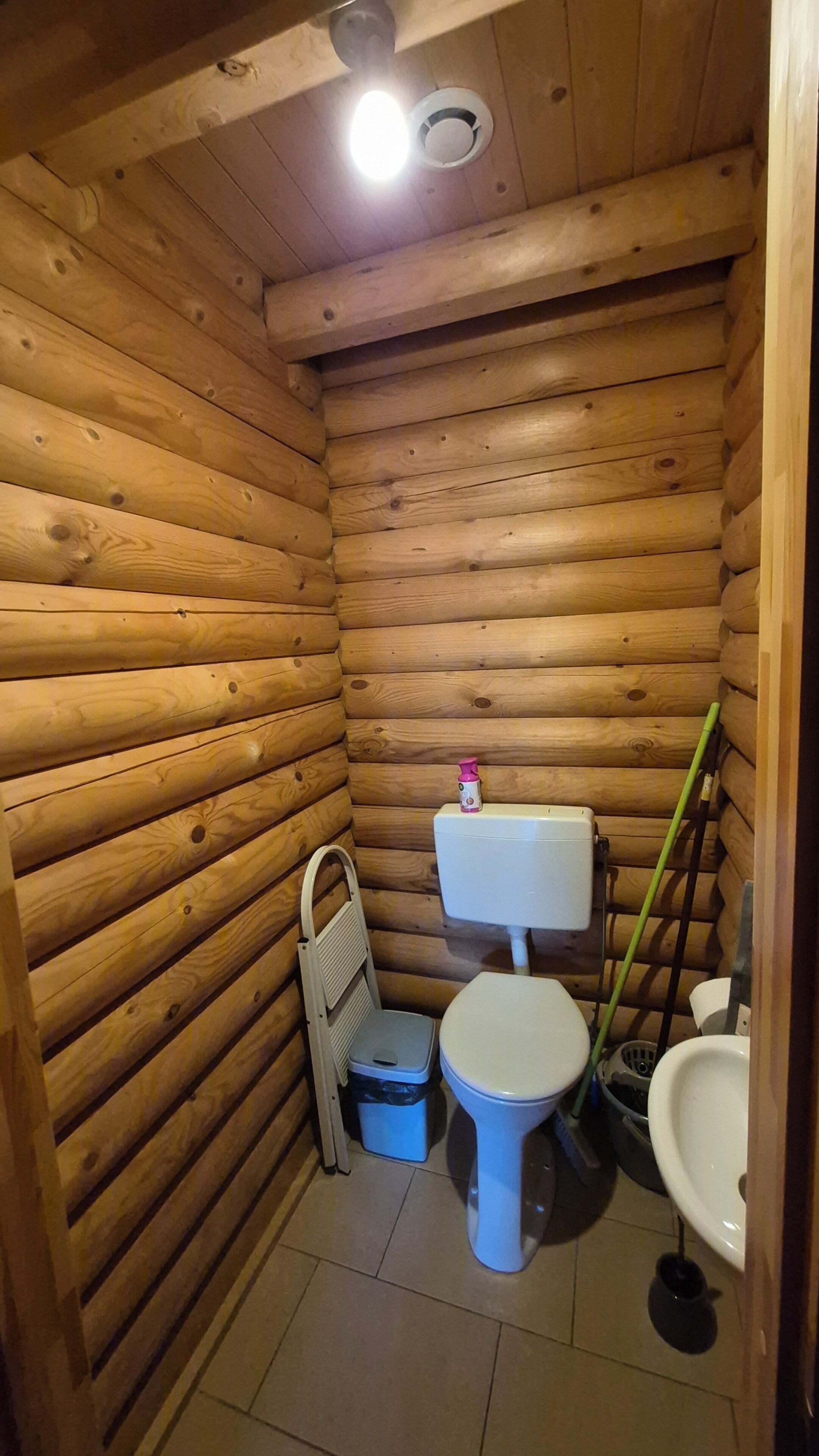 Un baño pequeño con paneles de madera, un inodoro, un lavabo y un cubo de basura.