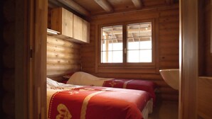 A cabin with two beds, wooden walls, a window, and a wooden cabinet.