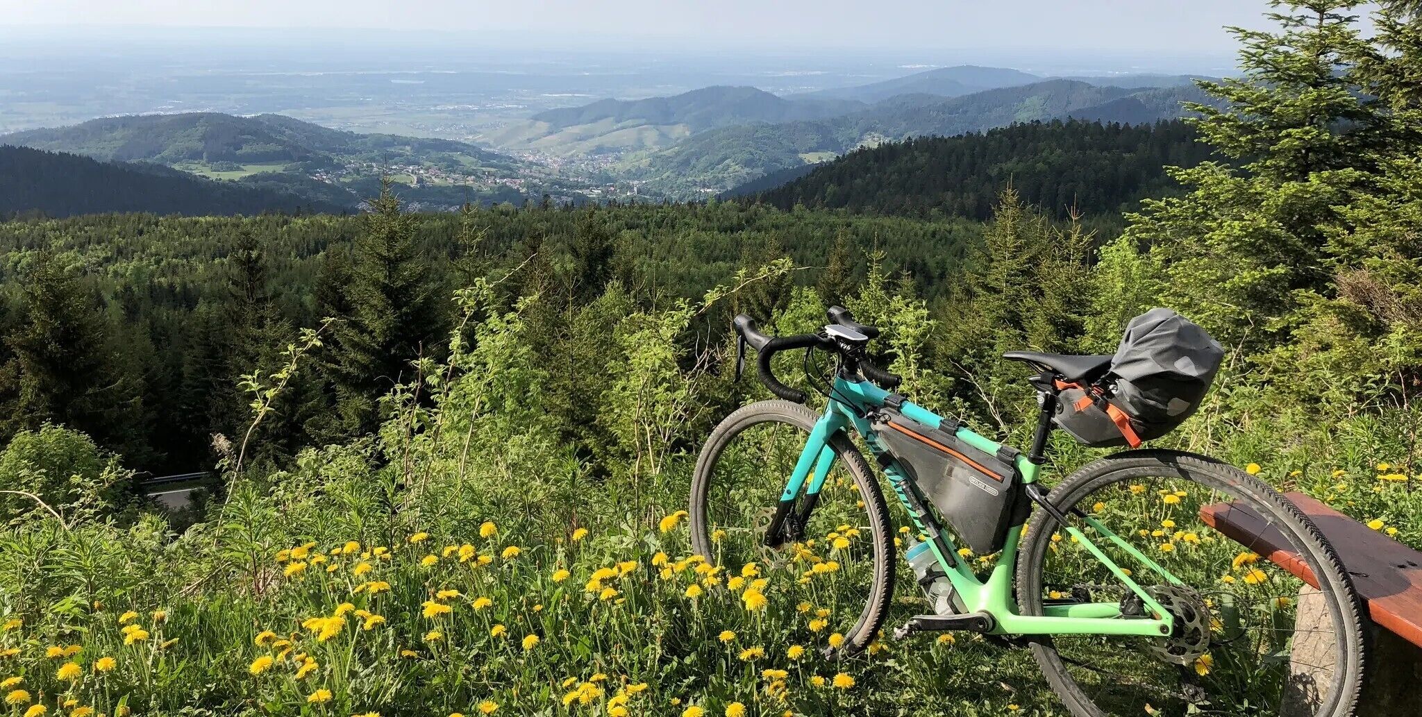 Una bicicleta de montaña estacionada en un sendero con vista a un valle y colinas boscosas al fondo.