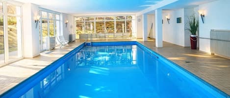 A swimming pool with clear glass walls, a wooden deck, and a view of the outdoors.